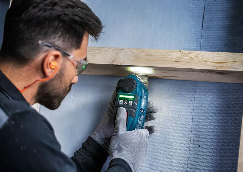 A person wearing safety equipment cuts through wood with a cordless multi-cutter.