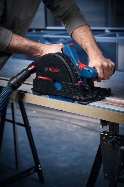 A person guides a cordless plunge saw along a metal rail to cut a wood panel.
