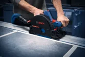 A person guides a cordless plunge saw along a track to cut a panel.