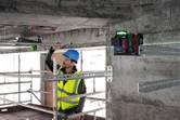 A person wearing safety equipment aligns metal rails using a laser leveling tool.