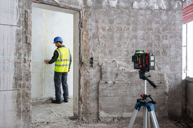 A person wearing safety equipment aligns a wall using a laser leveling tool.