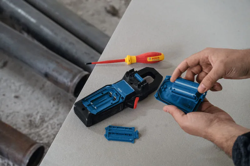 Person assembling a clamp meter battery compartment next to a screwdriver on a workbench.