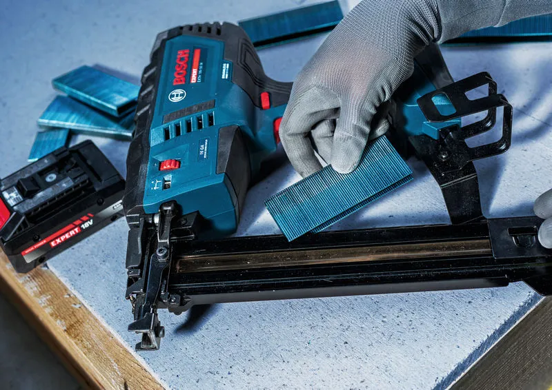 A person wearing safety equipment loads staples into a cordless wood stapler.