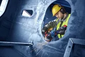 A person wearing safety equipment uses an angle grinder to cut through metal.