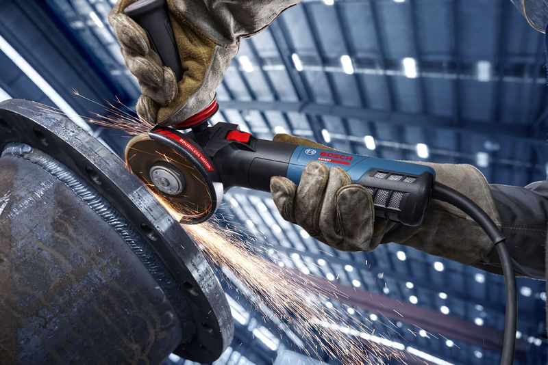 A person wearing safety equipment grinds metal with an angle grinder, creating sparks.