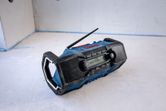 Portable jobsite radio with display and two speakers sits on a concrete floor.