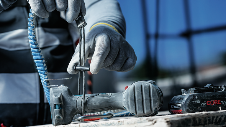 Person wearing safety equipment tightens a clamp on a drill at a construction site.