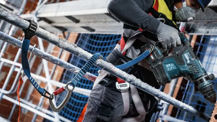 Person wearing safety equipment drills into concrete on scaffolding.