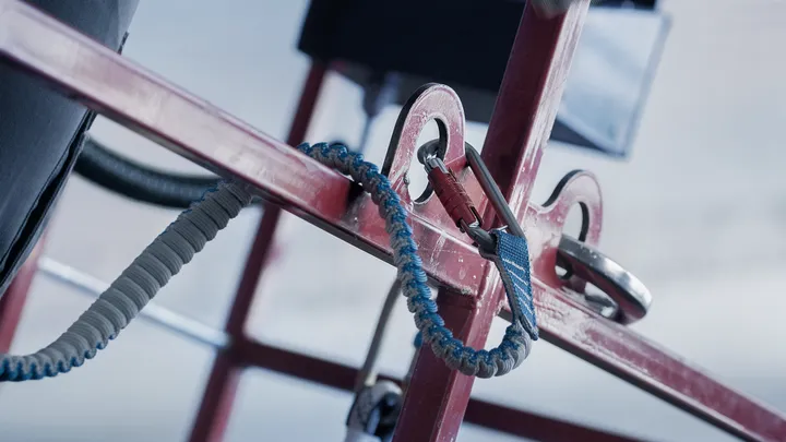 Safety lanyard secured to red metal framework for fall protection.