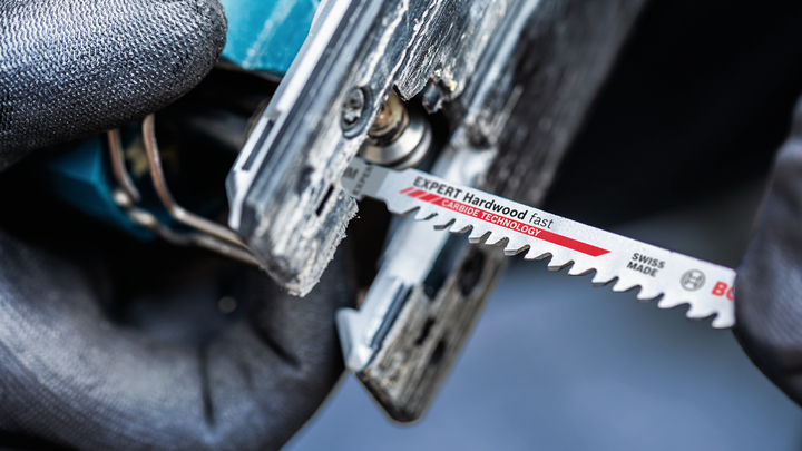 Person wearing safety equipment inserts a jigsaw blade into a power tool.