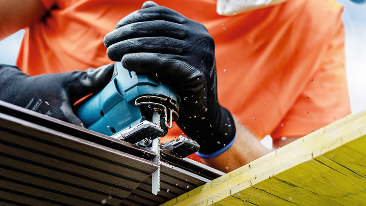 Person wearing safety equipment uses a jigsaw to cut through a piece of wood.