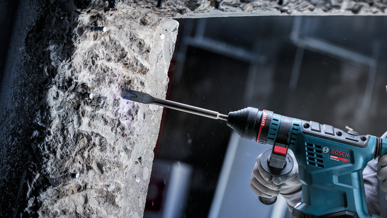 Person wearing safety equipment uses a power tool to chisel concrete.