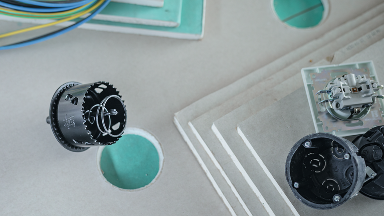 Hole saw creates circular cutouts in stacked drywall sheets.