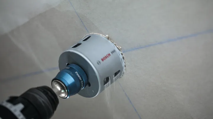 A hole saw drills into a marked wall surface.
