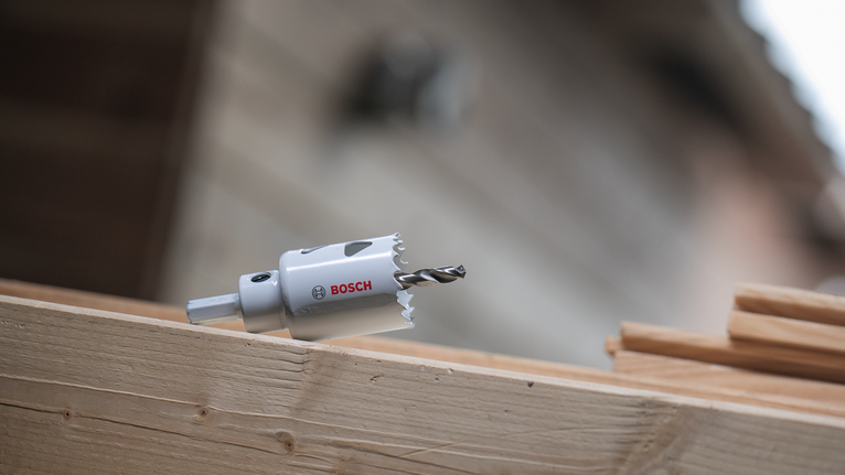 Hole saw drill resting on a wooden beam at a construction site.