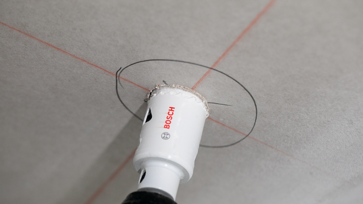 Hole saw cutting a circular opening in a ceiling marked with guide lines.