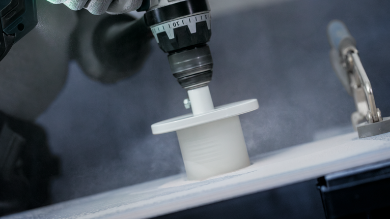 Hole saw drilling into a white material with fine dust visible.