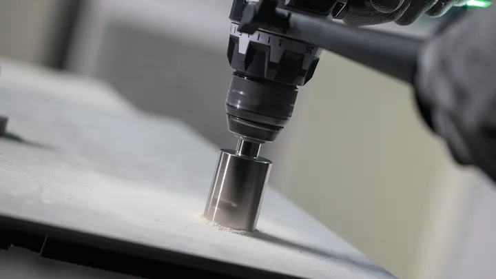 Rotary drill with hole saw attachment cuts through a flat stone surface.