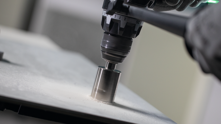 Rotary drill with hole saw attachment cuts through a flat stone surface.