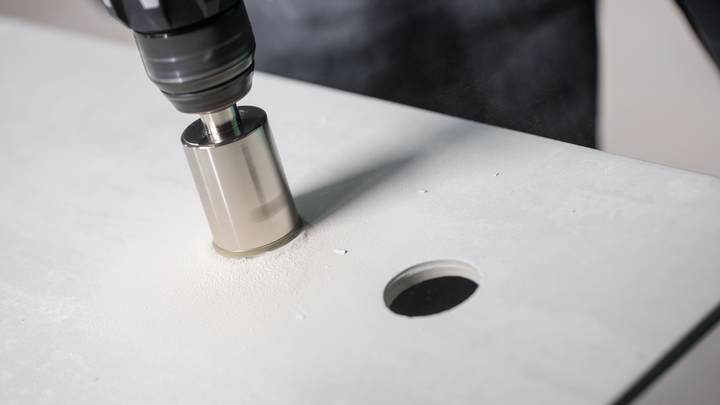 Hole saw drilling a circular hole into a flat white surface.