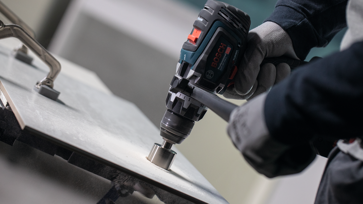 Person wearing safety equipment drills a hole into a tile surface.