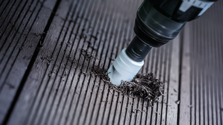 Hole saw drilling a hole in a wooden deck surface.