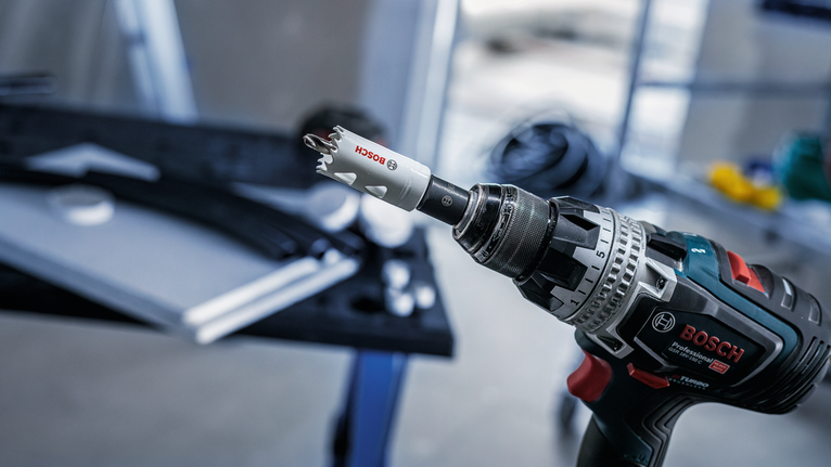 Cordless drill with a hole saw attachment positioned near a workbench.
