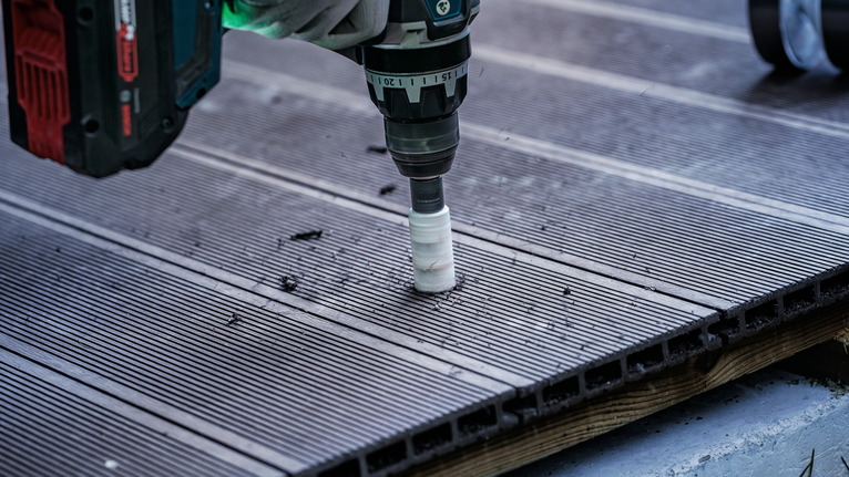 Person using a power drill to bore a hole in a grooved outdoor decking board.
