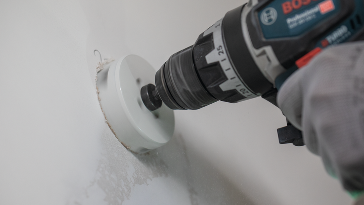 Person wearing safety equipment drills a circular hole into a wall.