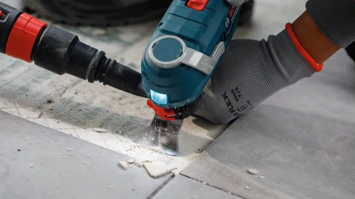 Person wearing safety equipment uses a power tool to cut through tile grout.