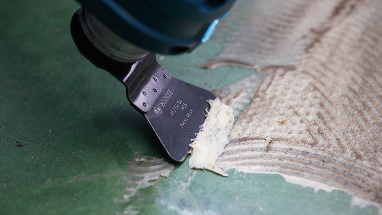 Oscillating tool removes adhesive residue from a green floor surface.