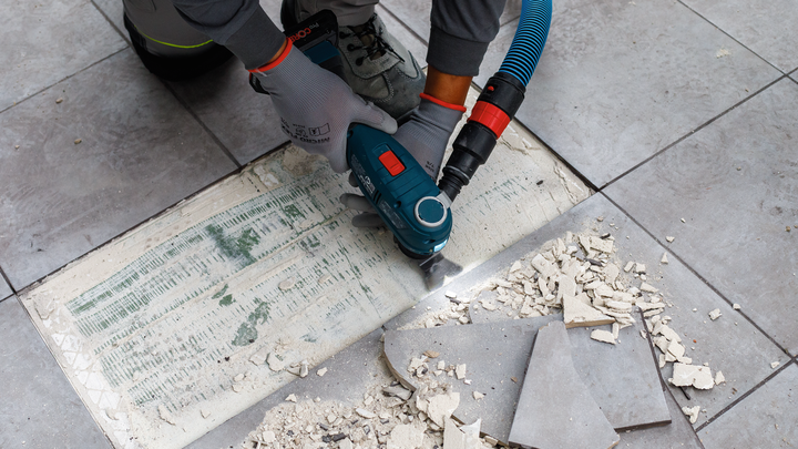 Person wearing safety equipment removes tile adhesive with a power tool.