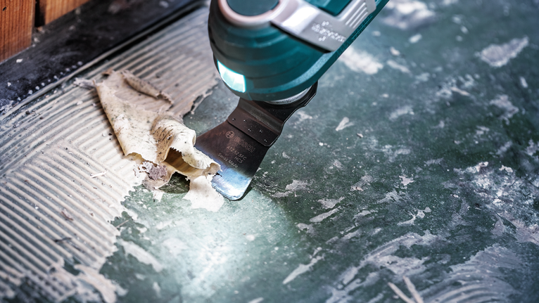 Oscillating tool scraping adhesive from a tiled floor.