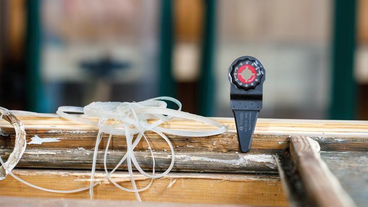 Oscillating tool blade attachment rests on a worn wooden surface with shavings.
