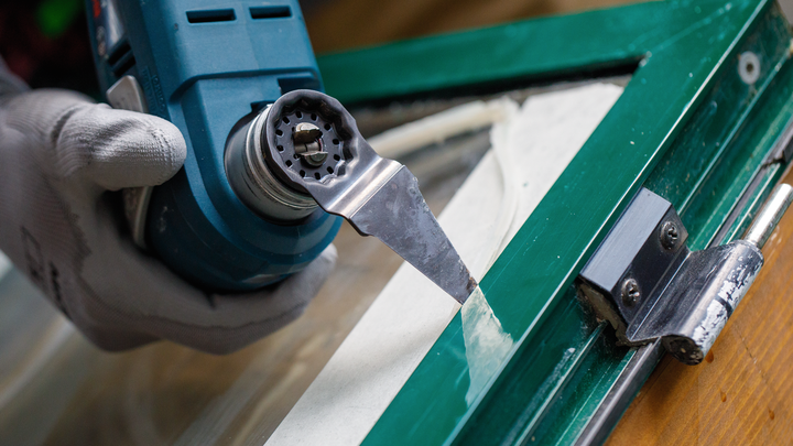 Person wearing safety equipment removes sealant from a window frame with a power scraper.
