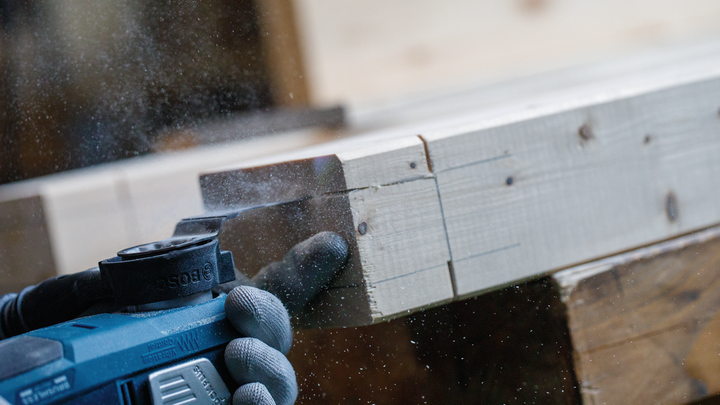 Person wearing safety equipment sands a wooden beam with a power tool.