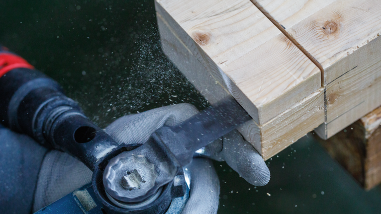 Person wearing safety equipment cuts wood with a power tool.
