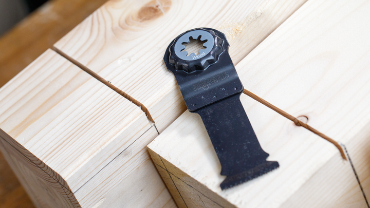 Oscillating saw blade placed on wooden beams with straight cuts visible.