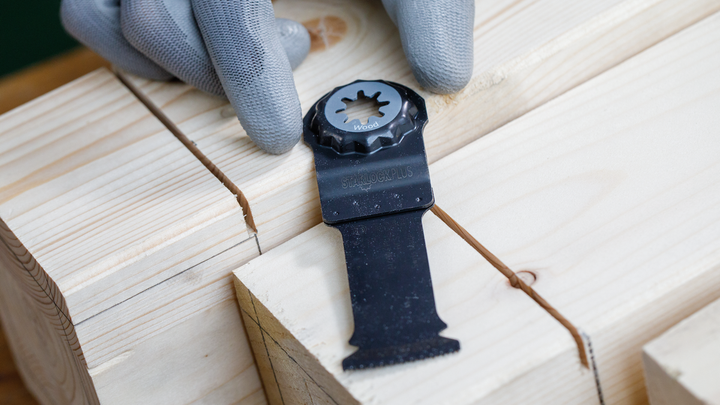Person wearing safety equipment places a saw blade next to a wooden joint.