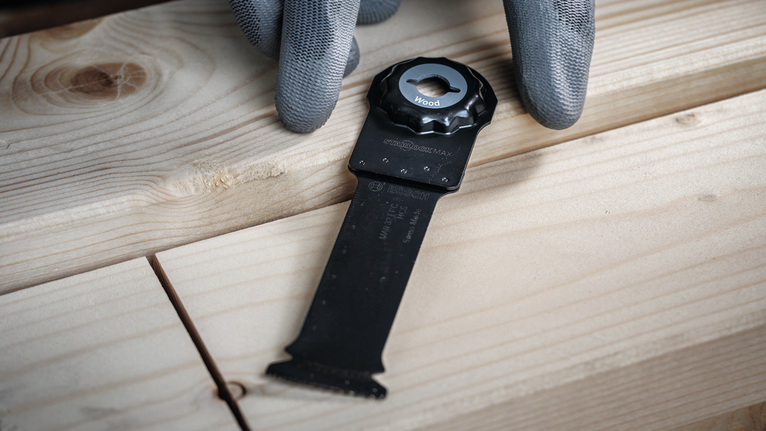 Person wearing safety equipment positions a cutting blade on a wooden surface.