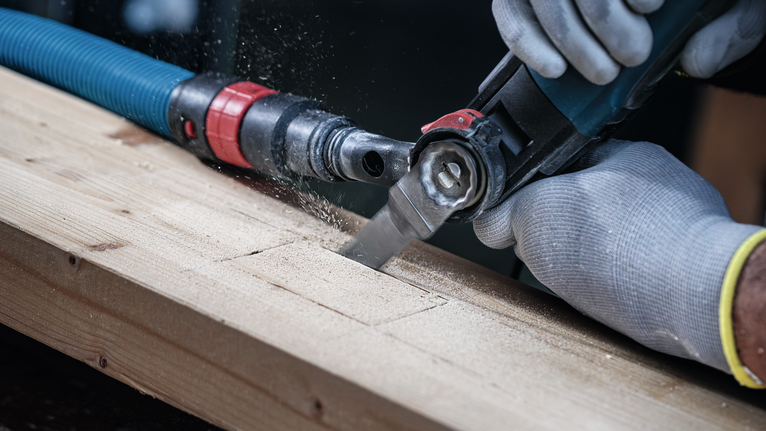Person wearing safety equipment uses a power tool to cut a rectangular notch in wood.