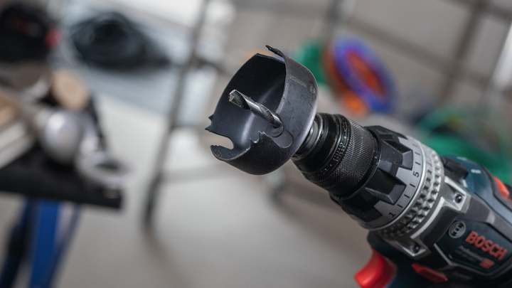 Close-up of a power drill with a hole saw attachment in a workshop.