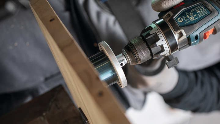 Person wearing safety equipment uses a power drill with a hole saw on wood.