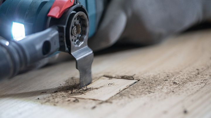 A person wearing safety equipment uses a multi-tool to cut a precise hole in wood.