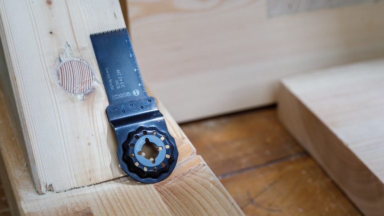 Oscillating saw blade positioned on a wooden beam with a circular cutout.