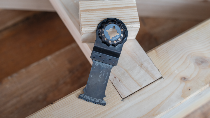 Oscillating saw blade resting on stacked wooden beams.