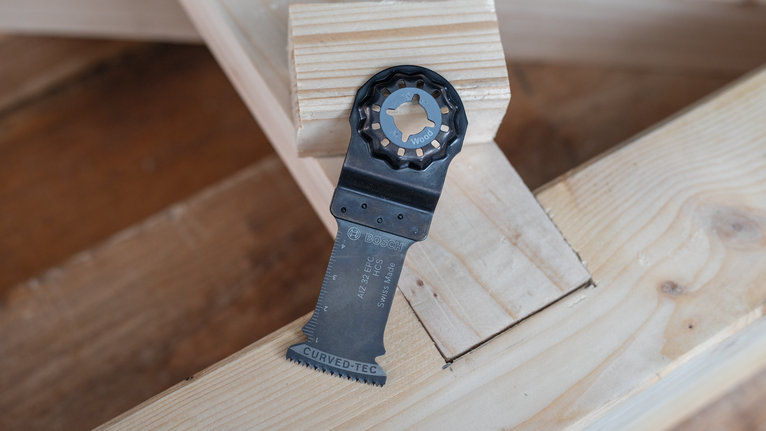 Oscillating saw blade resting on stacked wooden beams.