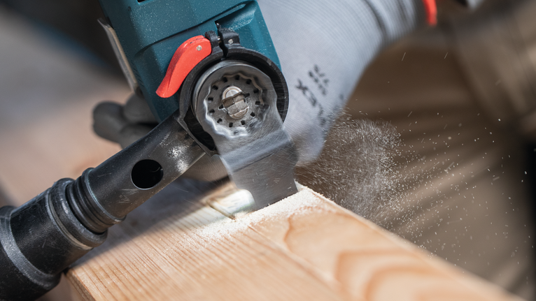 Person wearing safety equipment uses a power tool to cut a wooden plank.
