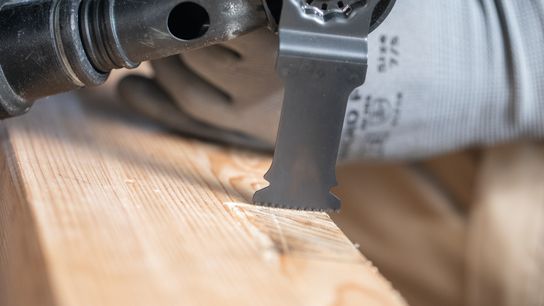 Person wearing safety equipment uses an oscillating tool to cut wood.