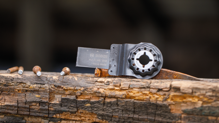 Oscillating saw blade attachment placed on a weathered wooden beam with nails.